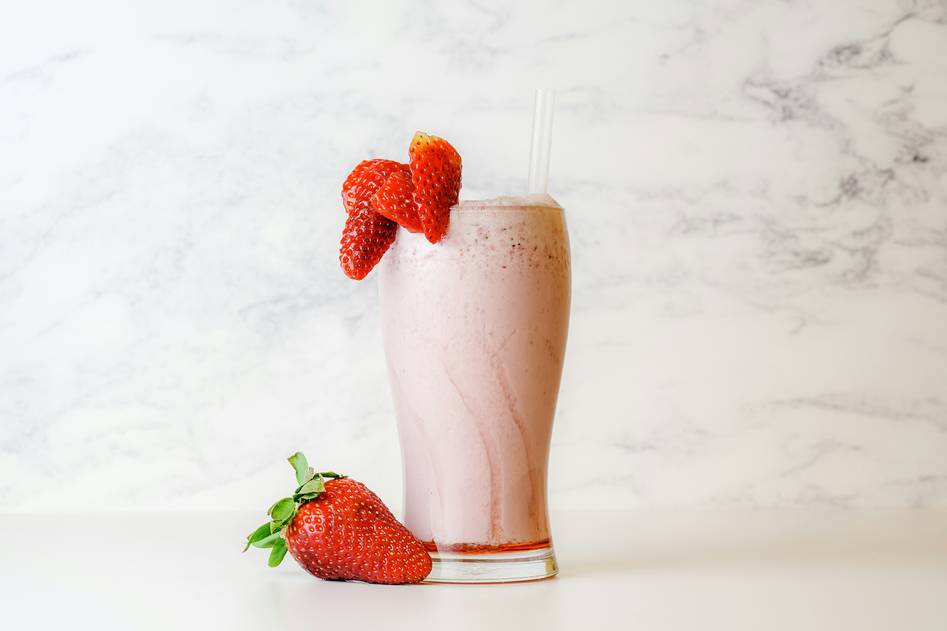 Woman smiling while holding a glass of green organic beauty shake near fresh produce