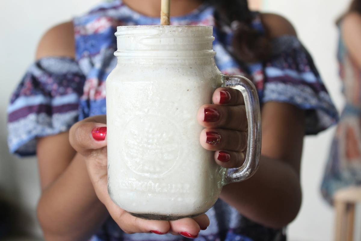 Woman blending organic plant protein smoothie with spinach, banana, and almond milk in kitchen